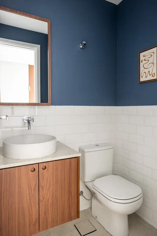 Lavabo revestido em azulejo tipo metrô azul, com cuba de apoio e espelho redondo